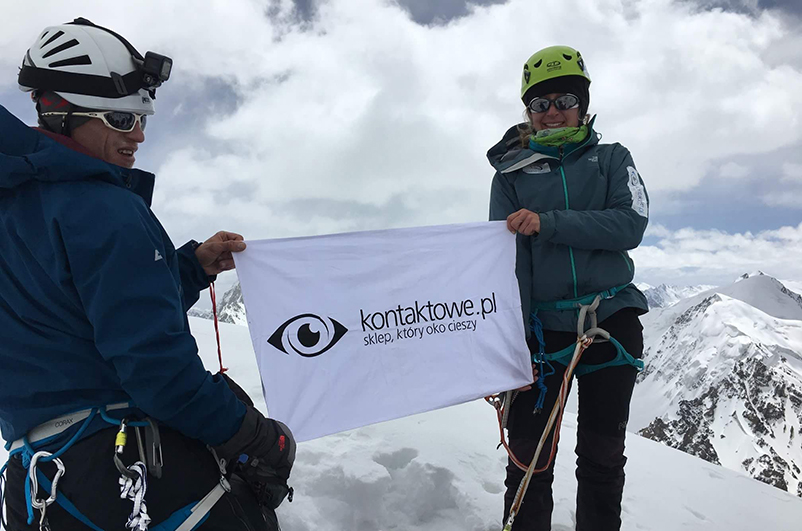 Dwóch uczestników wyprawy do Karakorum trzyma flagę kontaktowe.pl na tle gór.