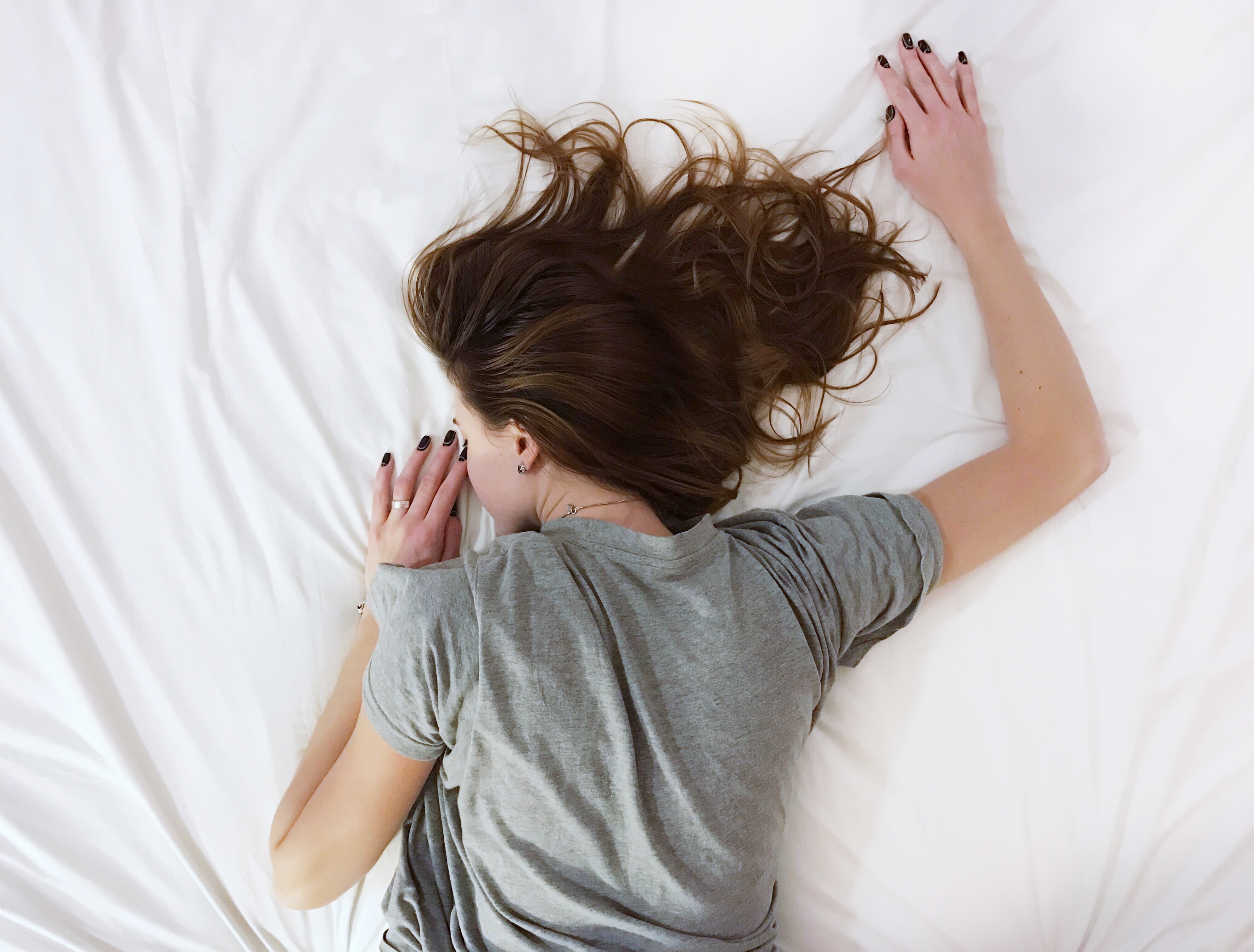 Zdjęcie przedstawia kobietę leżącą na łóżku na brzuchu. 